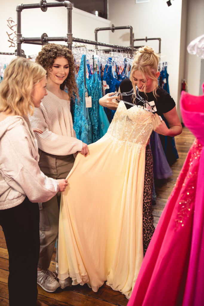 A candid behind-the-scenes shot of models discussing dress options inside Spotlight Bridal, highlighting the variety of styles available for Prom 2026. prom dress accessories
