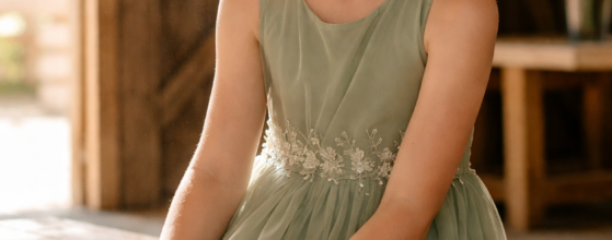 Flower girl dresses Ralston NE young girl in sage green chiffon flower girl dress seated inside rustic barn wedding venue at midday