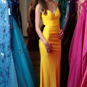 Make an unforgettable entrance in this bold yellow prom dress, featuring flattering ruching and a head-turning silhouette. A girl smiling in a fitting room while trying on homecoming dresses near Council Bluffs IA